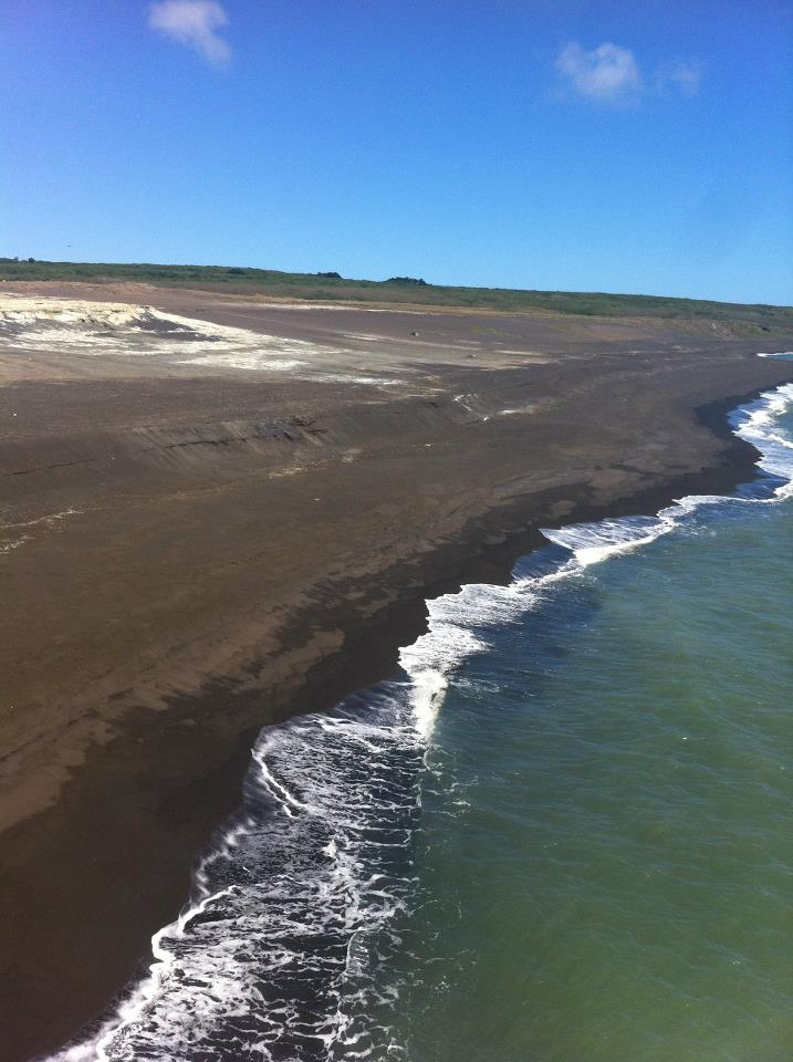 Dark sand along Invasion Beach, Iwo Jima, with surf breaking beside the shoreline.