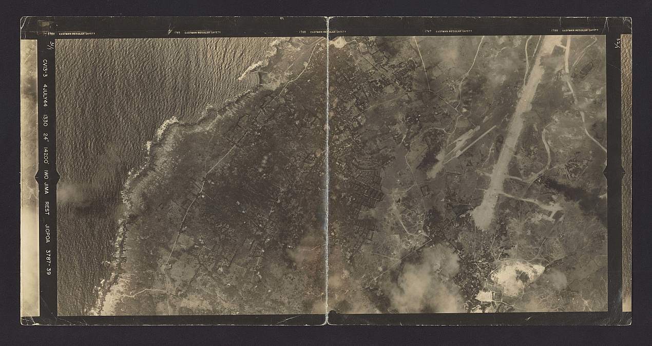 Historical aerial image labeled Iwo Jima, showing a coastline, roads, and airfield infrastructure.